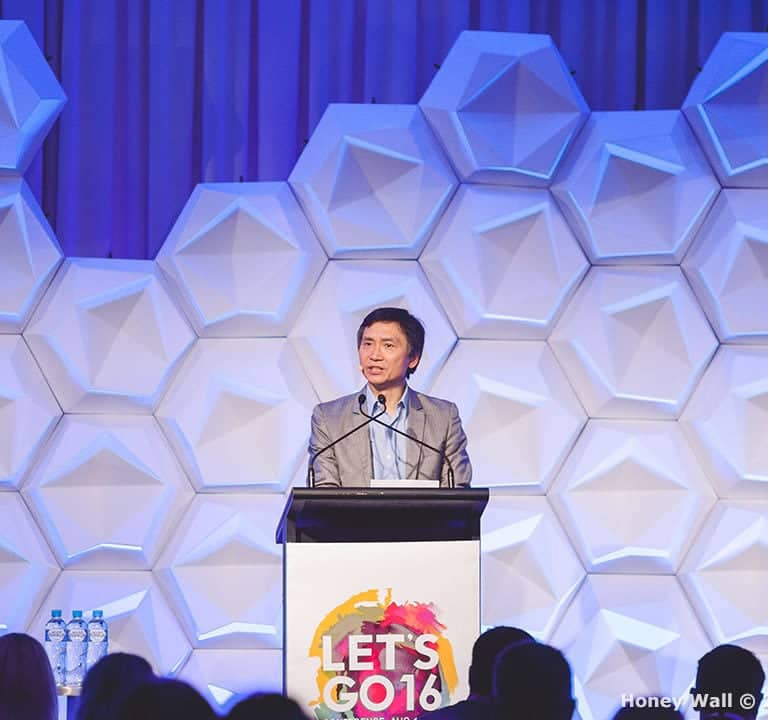 A man speaks at a podium with the sign