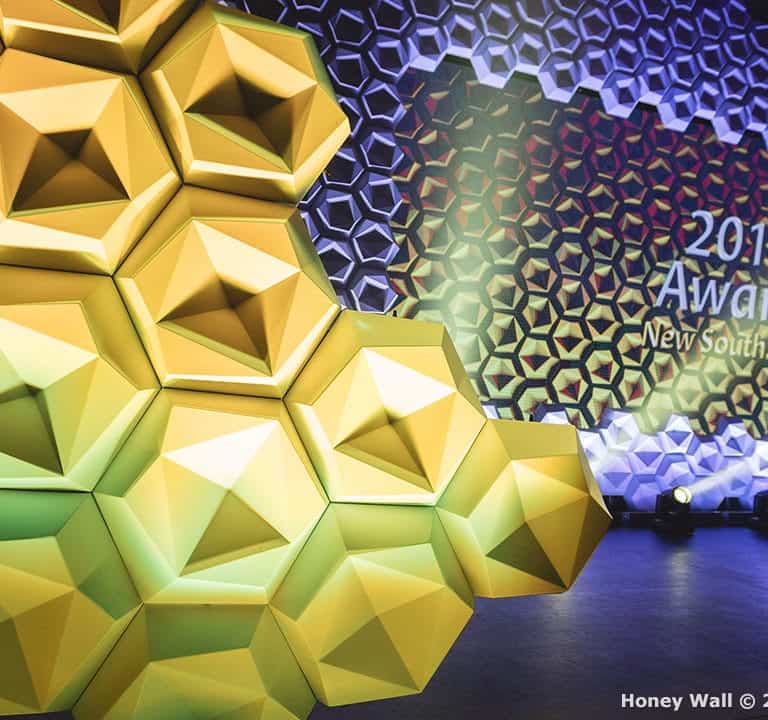 An awards stage with a hexagonal honey wall backdrop. Text on the wall says