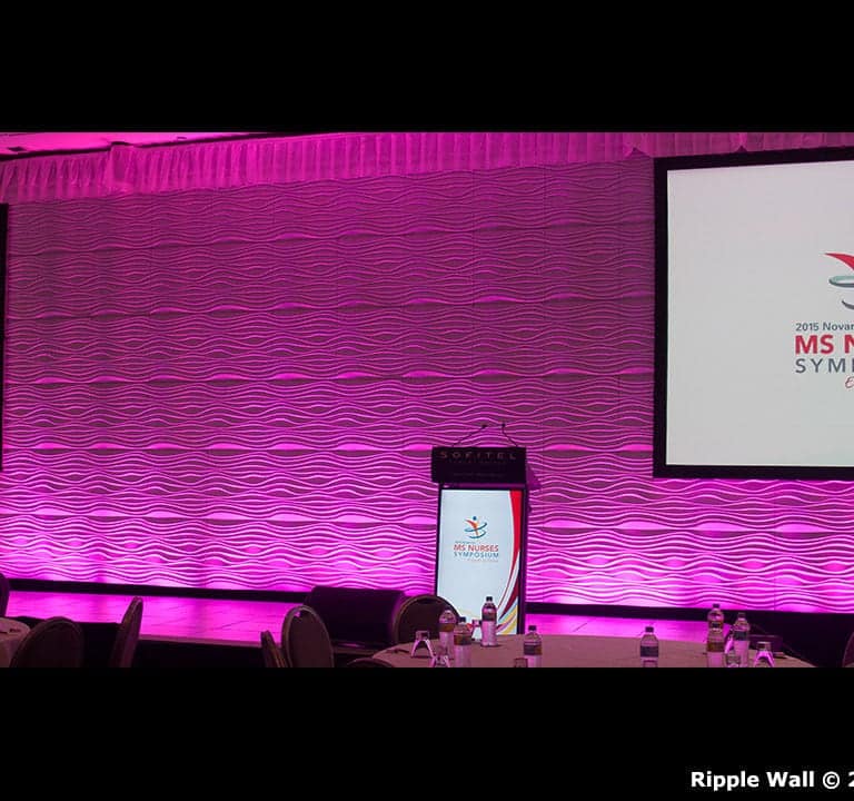A stage setup for the MS Nurses Symposium 2017 featured two large screens displaying the event's logo, a podium in the center, and ripple wall modular backdrops illuminated in pink.