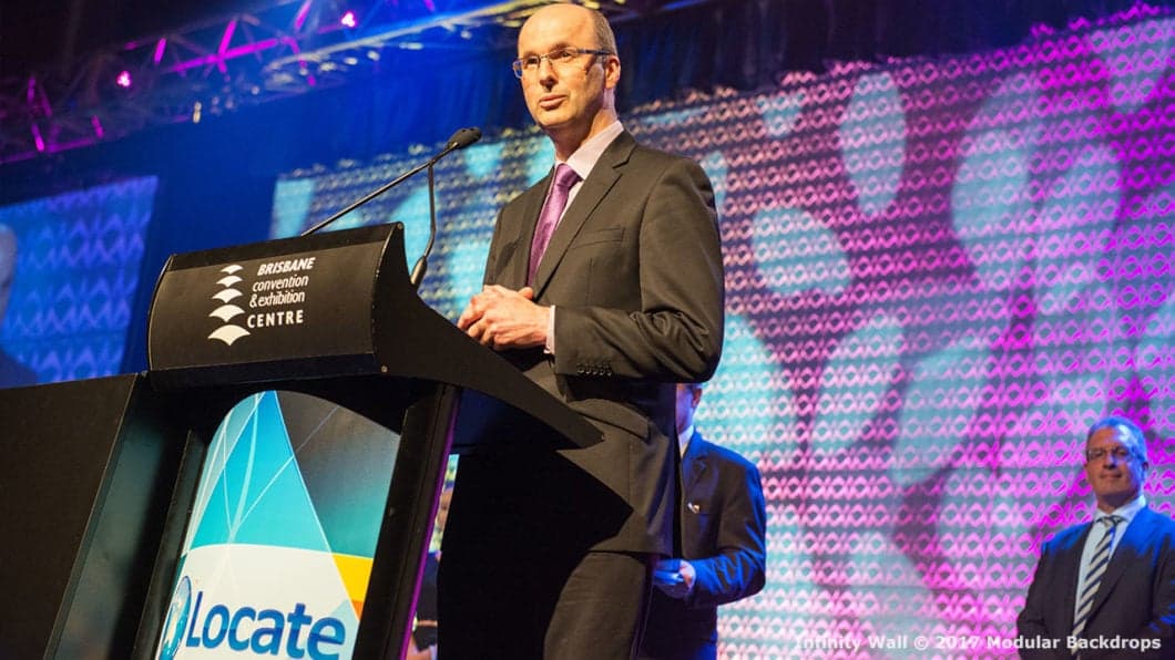 A man in a suit speaks at a podium labeled 