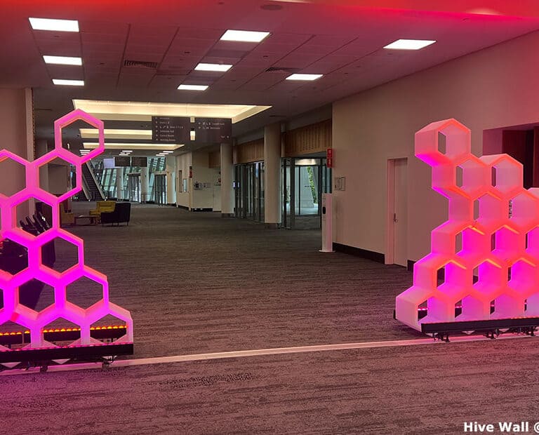 A hallway with two illuminated hexagonal structures resembling Hive Modular Panels on either side, casting a serene pink glow.