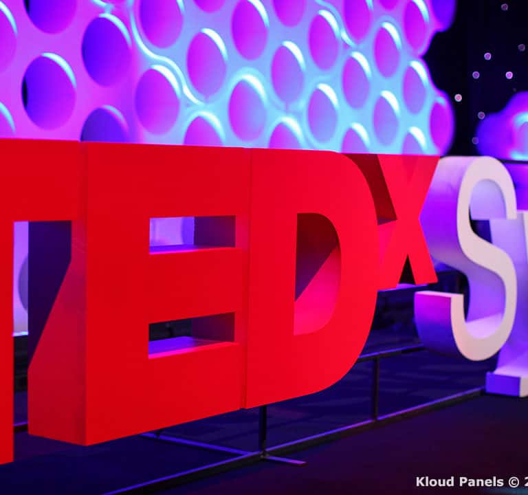 TEDxSydney sign displayed against a backdrop of circular patterns illuminated in purple. .